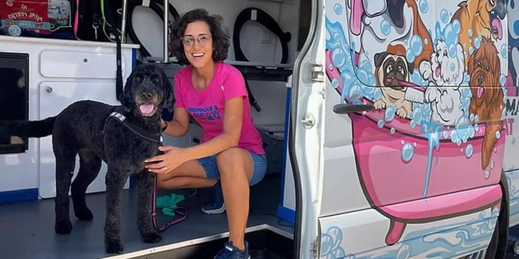 Benefits of mobile pet grooming. Groomer sitting inside grooming van with a freshly groomed dog